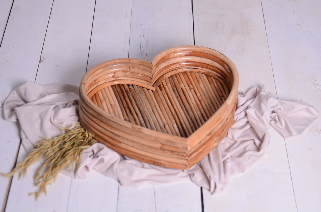 Rattan Heart Bowl for newborn photography prop, placed on a white wooden floor with a soft beige fabric and dried wheat for a natural, rustic aesthetic.