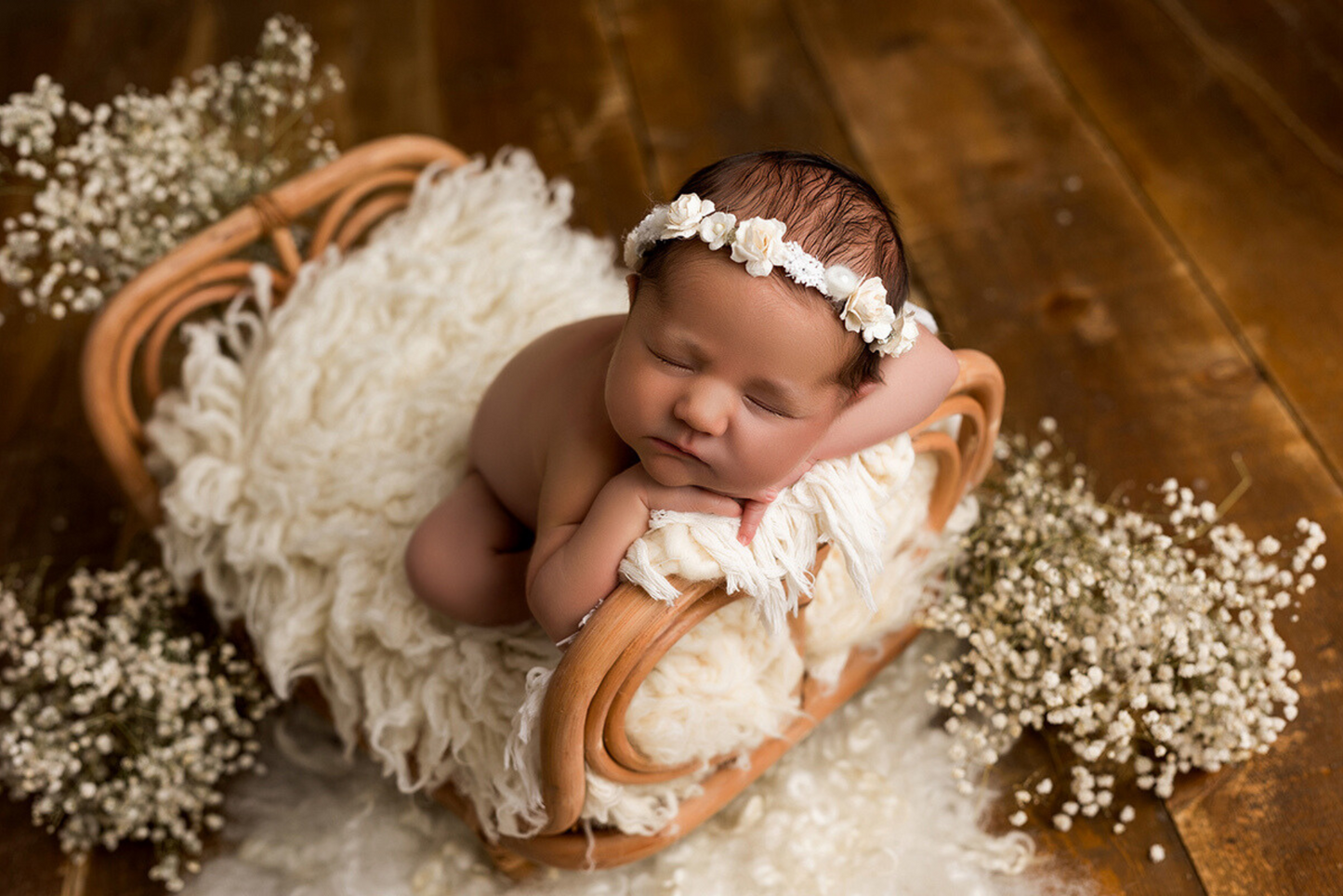 Cherubic newborn in lace dress, cradled in a rustic rattan bed with cream pillows.