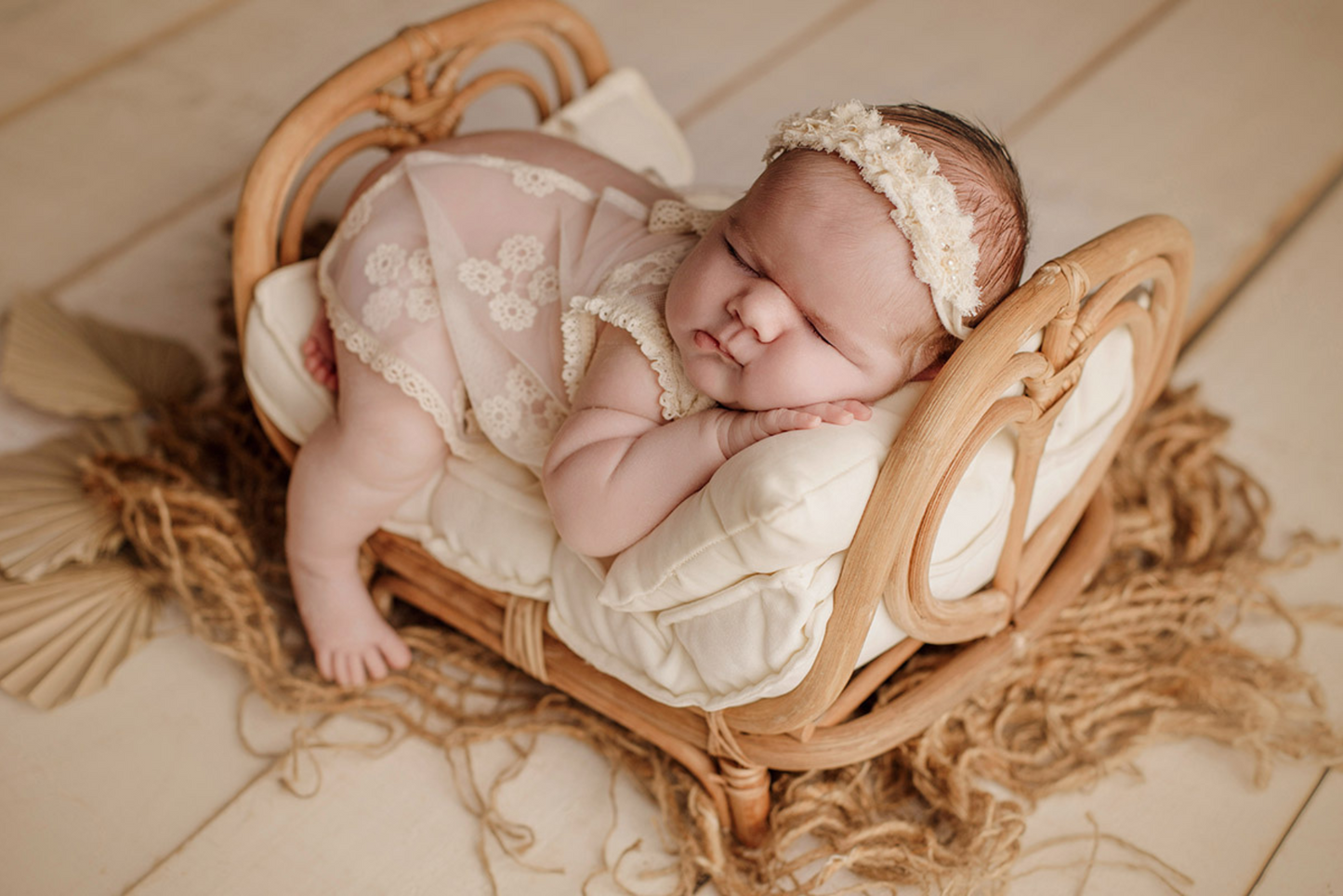 Newborn in a cozy rattan basket with fluffy white blanket, floral headband, and gentle backdrop.