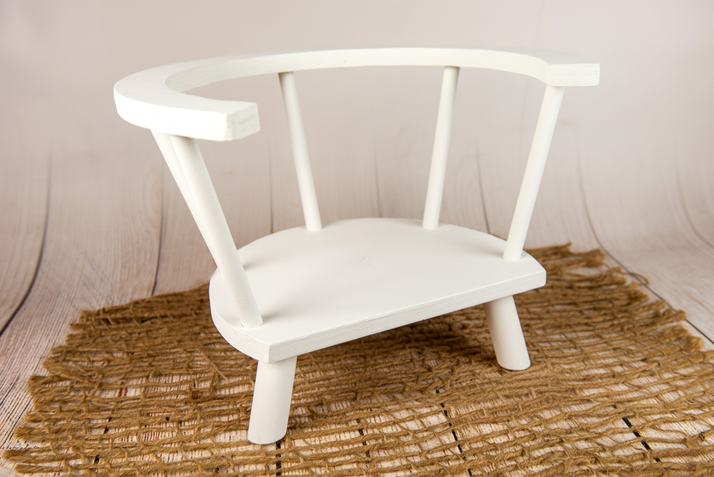 Side view of white wooden orbit chair newborn and toddler photography prop on rustic woven jute mat.