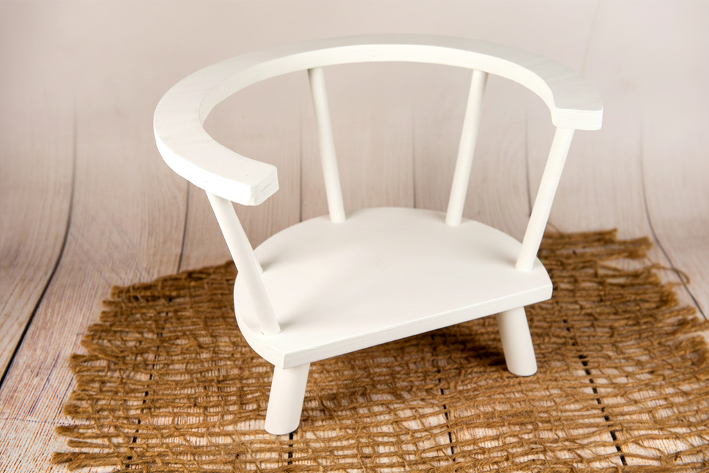 Angled view of white wooden orbit chair newborn and baby photography prop styled with rustic jute mat.