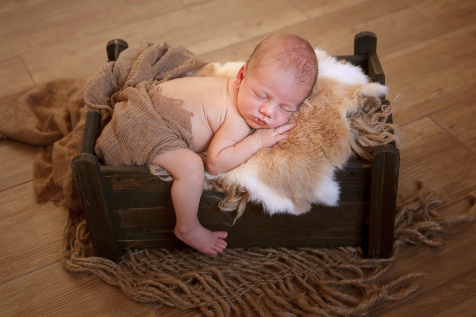 Baby sleeping peacefully in a fluffy cream wrap on a rustic wooden bed, a serene newborn photography prop.