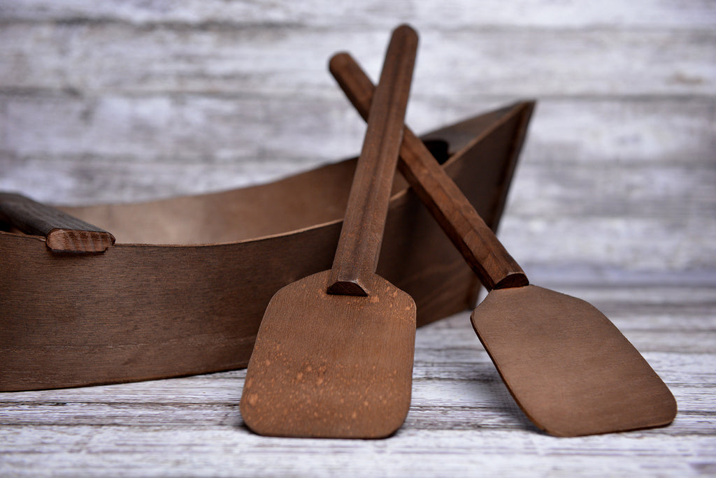 Dark stained boat newborn photography prop with two wooden oars on a distressed gray wood floor