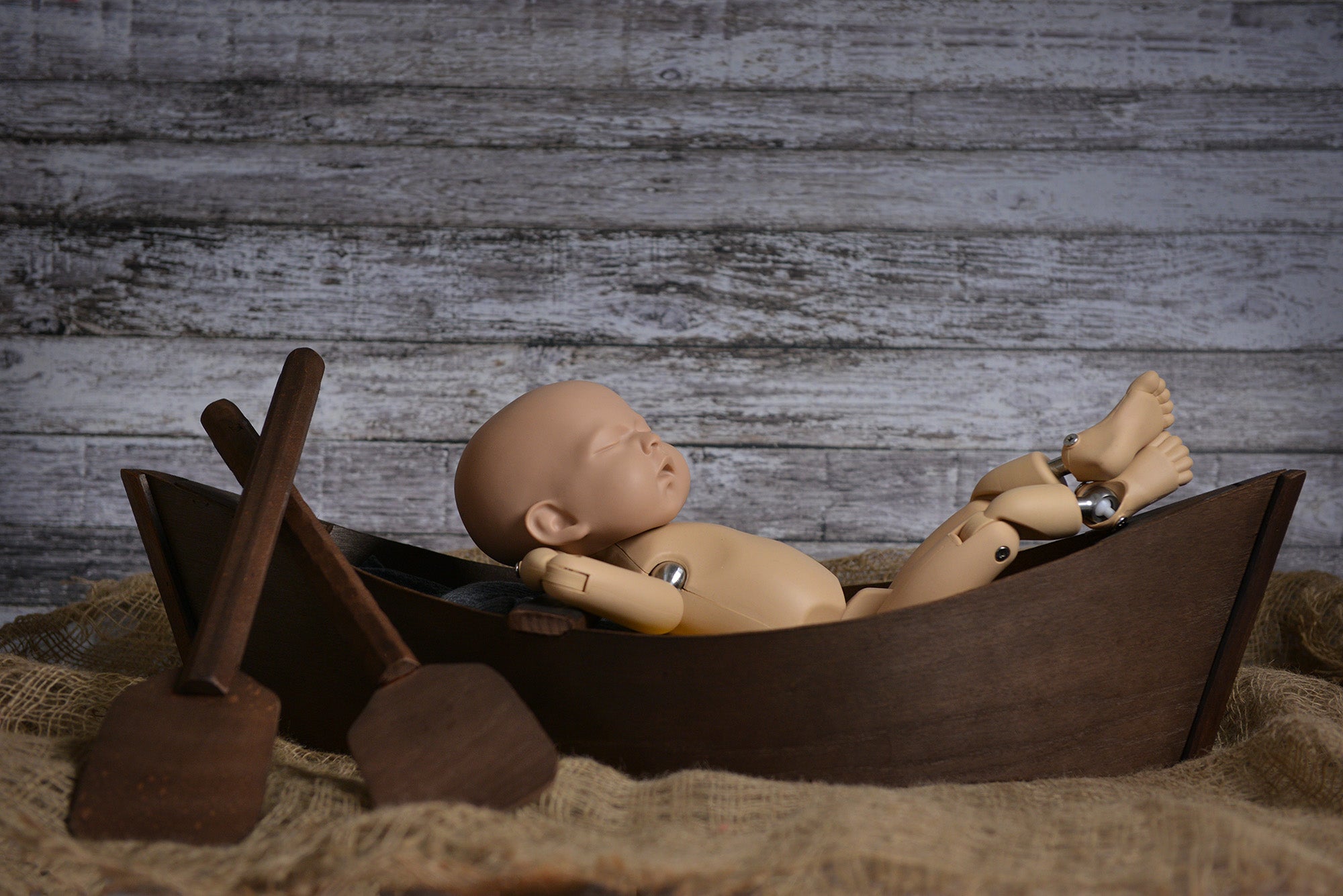 Wooden boat newborn photography prop styled with oars and a posing baby on burlap