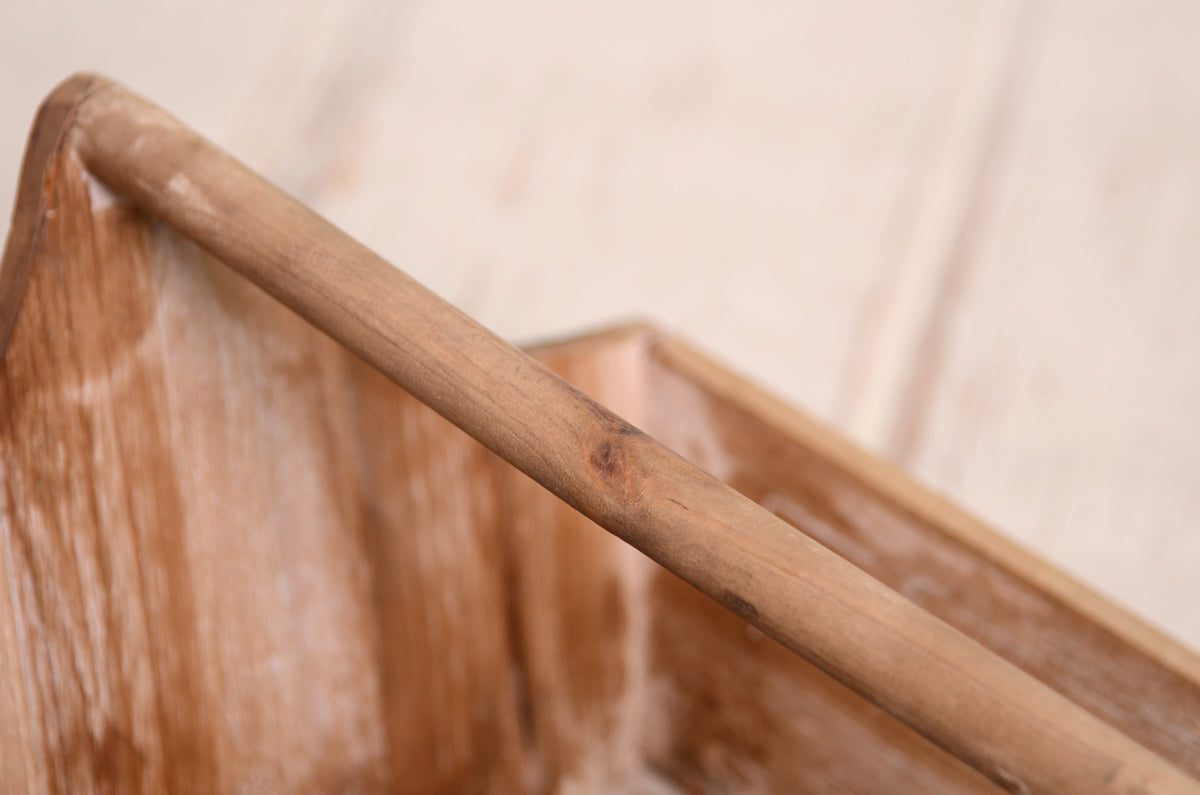 Wooden basket with a curved handle and weathered finish, styled with greenery and wool textures for newborn photography setups.