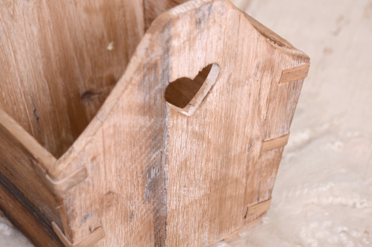 A charming wooden crate with heart-shaped details, used as a newborn photography prop, styled on soft wool fabric with greenery accents.