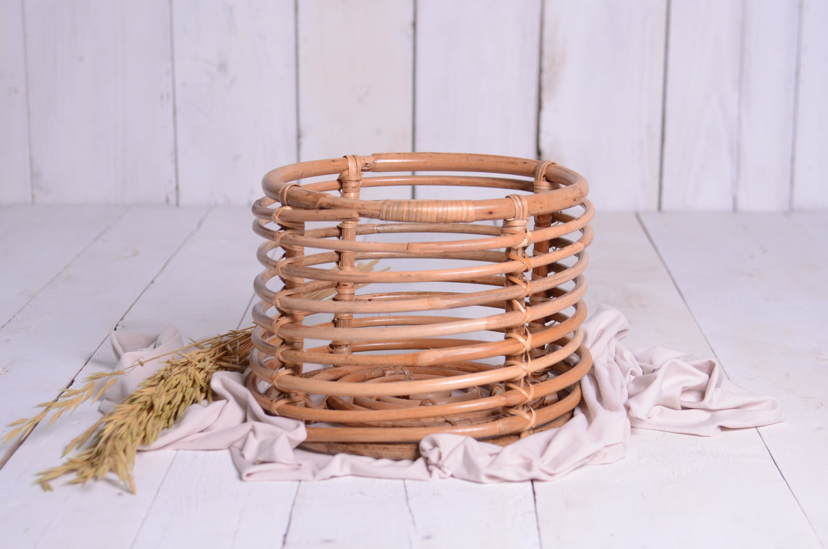 Rustic rattan bowl newborn photography prop set on a soft cream fabric with dried wheat, creating a cozy, farmhouse-inspired setup.