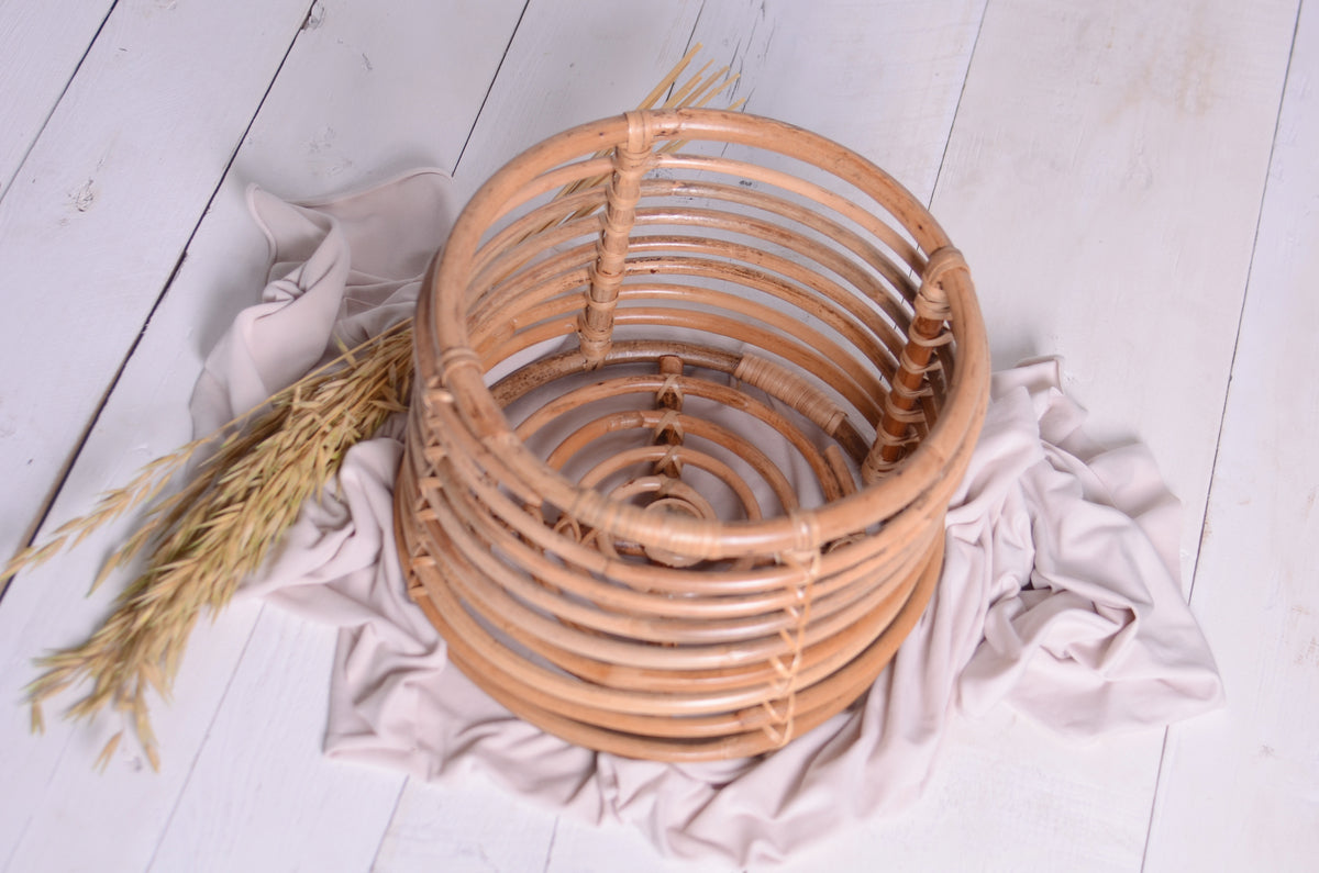 Handwoven rattan bowl newborn photography prop, styled with neutral draping and dried wheat on a white wooden backdrop.