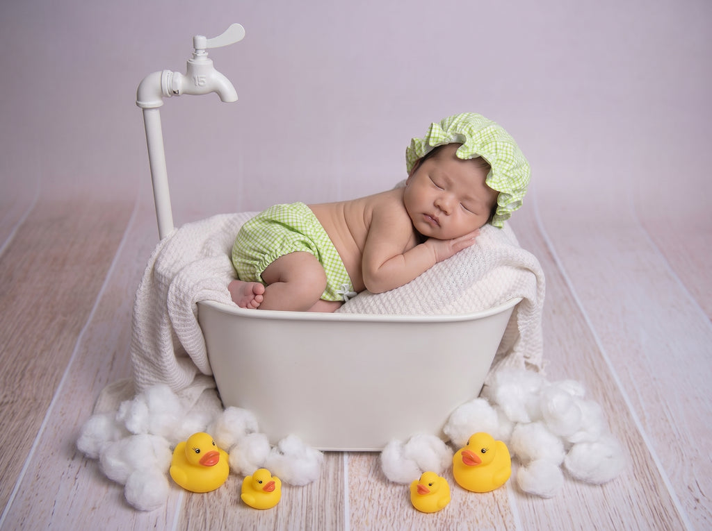 Newborn baby in a bathtub with rubber ducks and a green outfit newborn spa-theme photoshoot