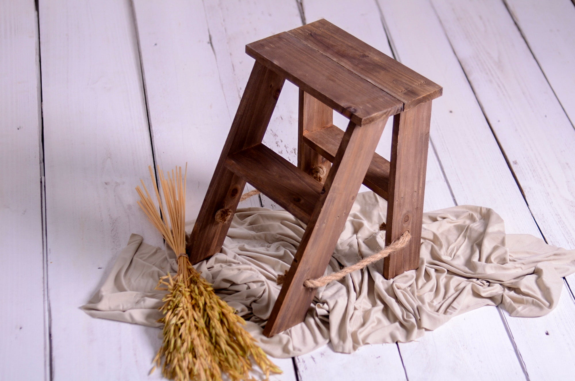 Top-down view of vintage wooden ladder prop styled with beige fabric, perfect for milestone shoots and cake smash sessions.