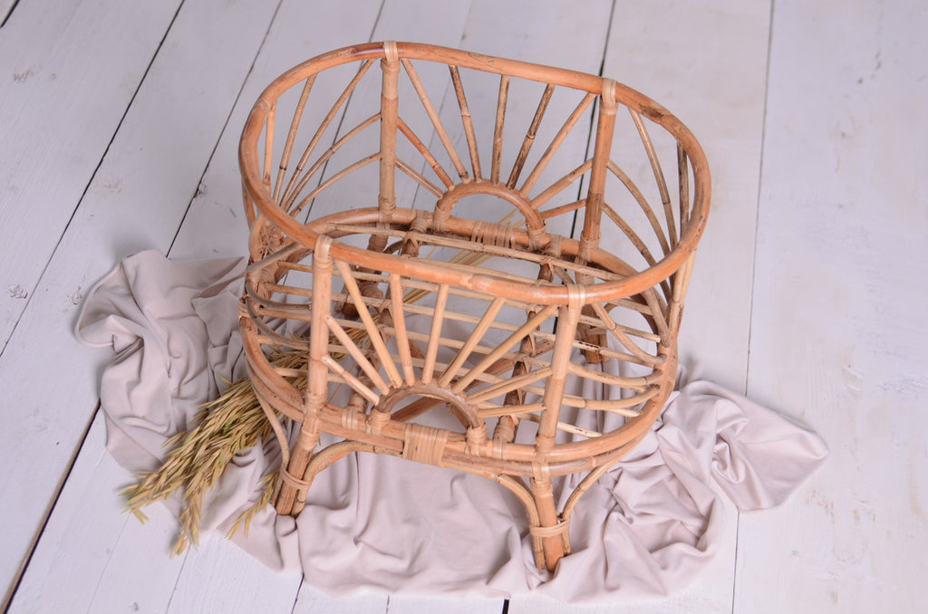 A full view of the Sun-Kissed Rattan Cradle styled with a white fabric base and delicate dried florals, emphasizing its boho-inspired charm as a newborn photography prop.