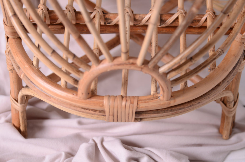 The base of the Sun-Kissed Rattan Cradle, with a soft white fabric beneath, highlighting its sturdy yet delicate rattan design. A versatile newborn photography prop with a timeless look.