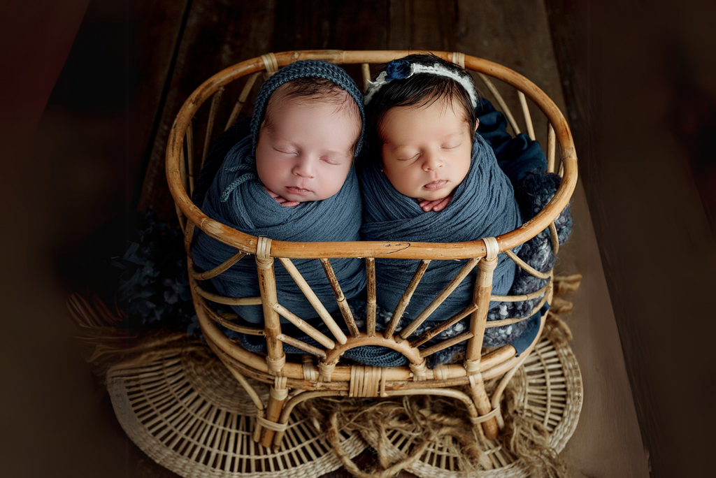 Two newborns snugly wrapped in deep teal swaddles, resting inside the Sun-Kissed Rattan Cradle. The intricate rattan design frames them beautifully, set against a warm-toned background. A charming newborn photography prop for twin sessions.