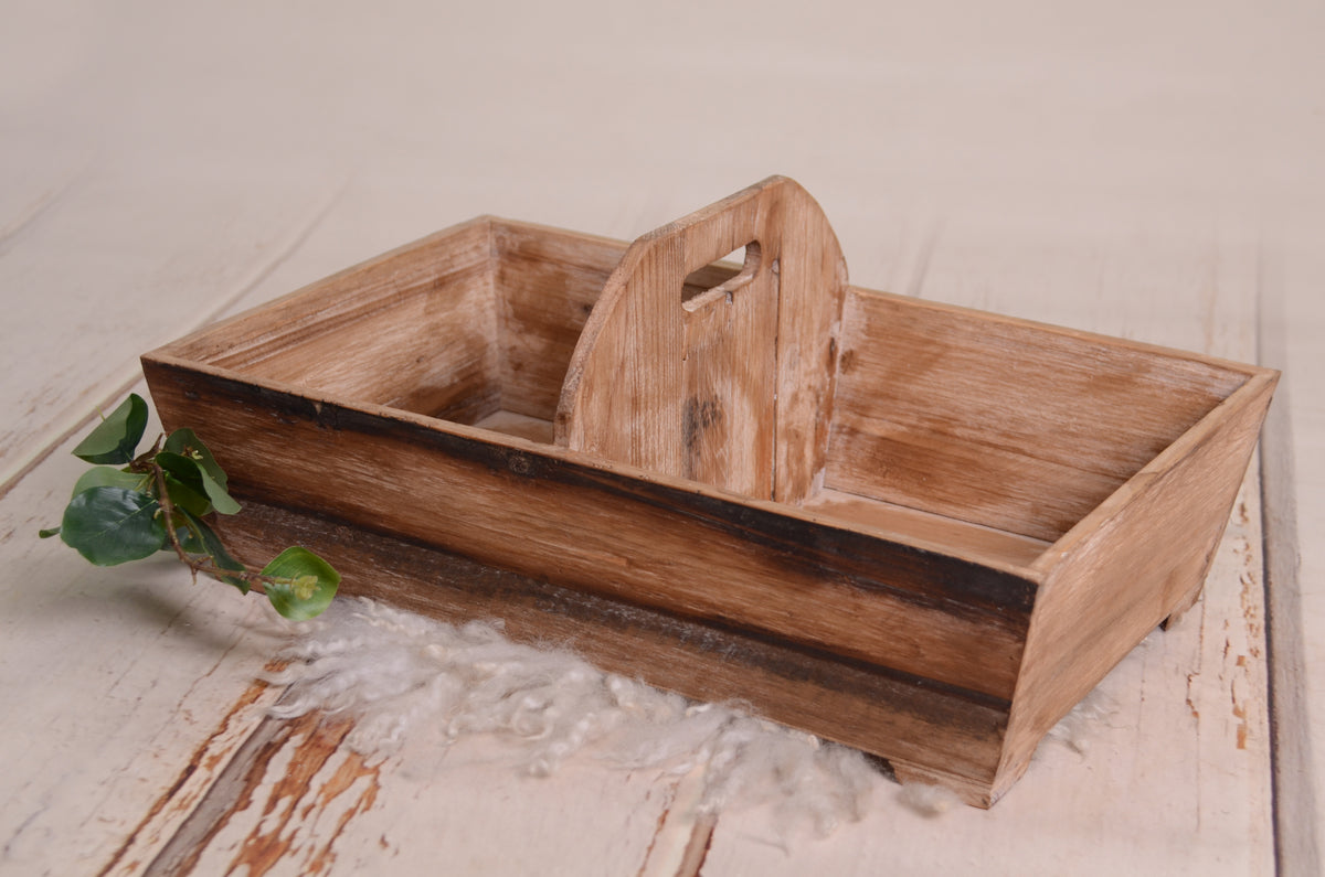 Rustic wooden twin snuggle crate, perfect as a newborn photography prop. Features a distressed brown finish with a central divider, ideal for posing twins. Styled on a white wooden floor with soft wool and greenery for a cozy, natural look.