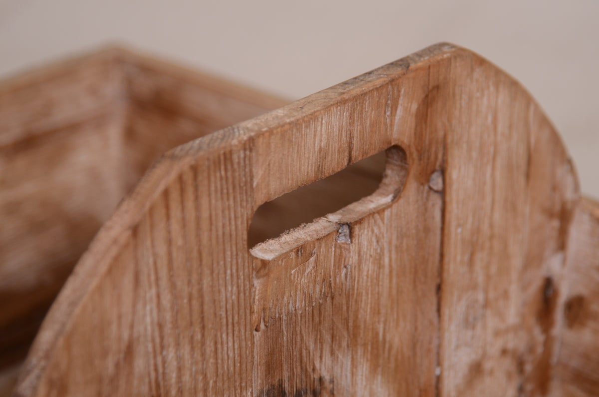 Close-up of the handle on a rustic wooden twin snuggle crate, a charming newborn photography prop. The distressed brown wood showcases its vintage appeal, with a smooth, curved cutout for easy handling. Styled against a white wooden floor with soft wool and greenery for a cozy, organic feel.