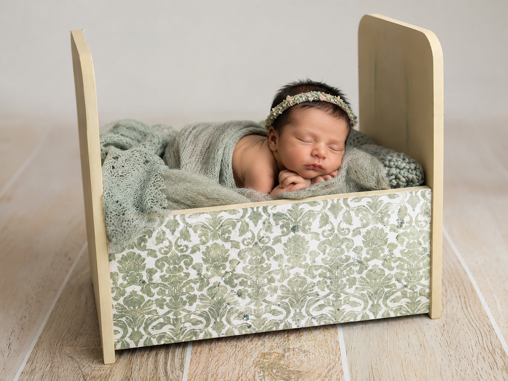 Newborn baby sleeping in a small crib with green bedding and headband.