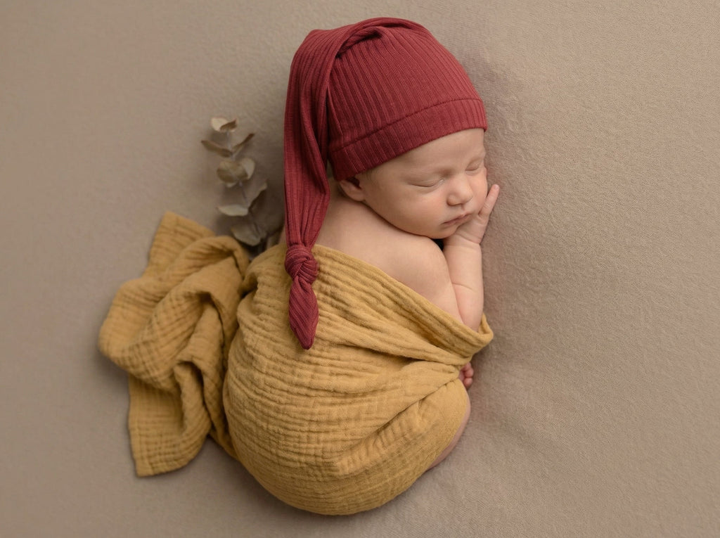 Sleeping newborn wrapped in mustard swaddle with ribbed knot sleepy cap newborn photography clothing.