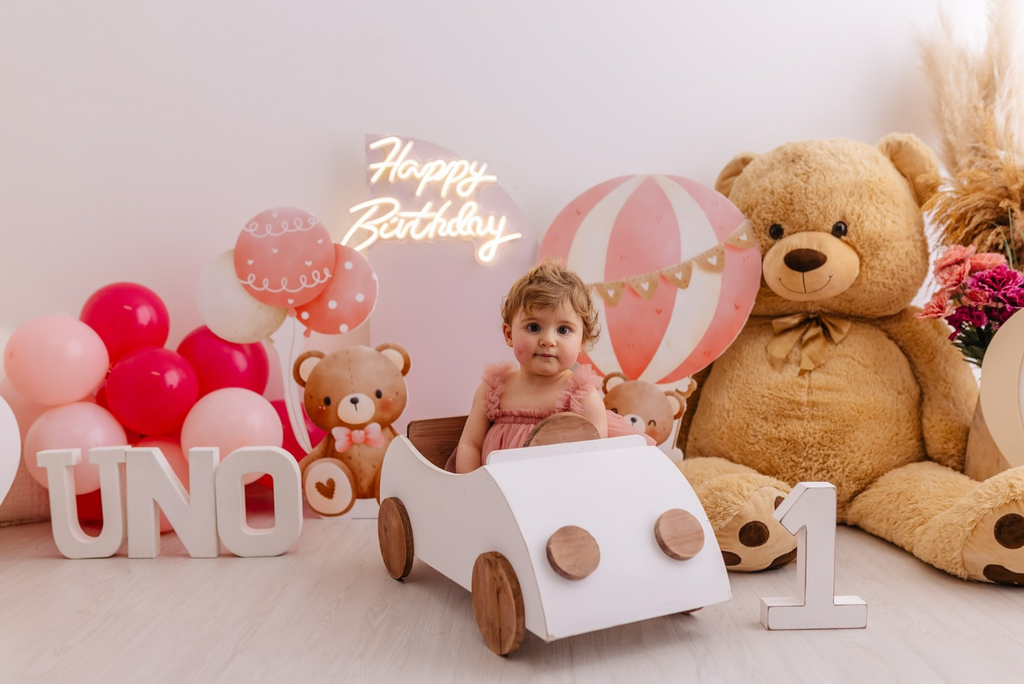 Baby in white wooden Beetle Cabrio newborn photography prop, surrounded by teddy bears and balloons.
