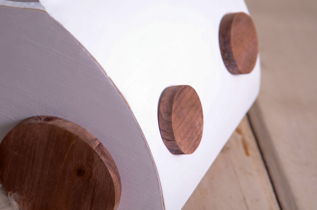 Close-up of a wooden VW Beetle-inspired newborn photography prop, focusing on the front details. The white-painted body contrasts with the natural wooden circular accents resembling headlights.