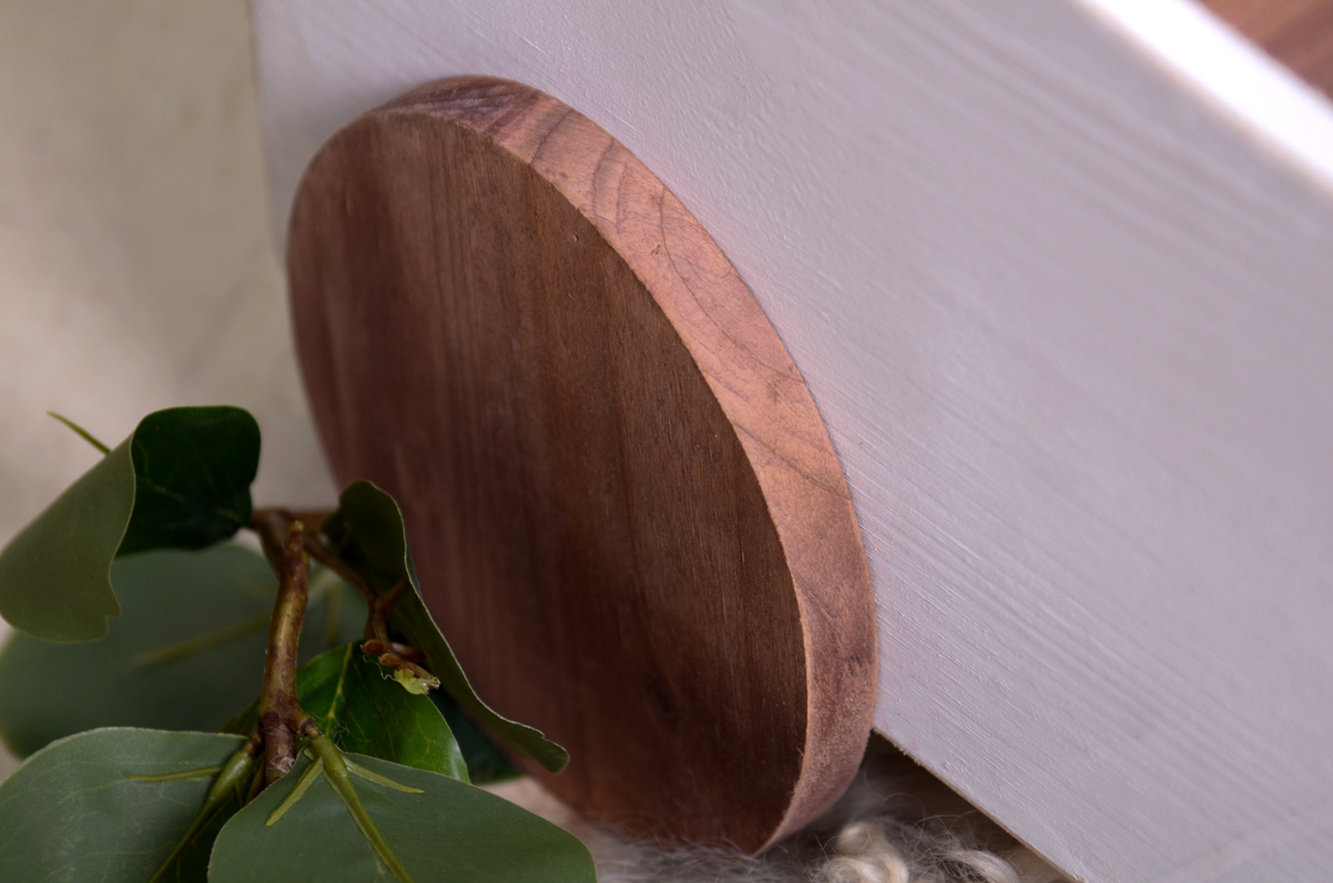 Close-up of the wooden wheel on the side of the VW Beetle-inspired newborn prop. The natural wood grain is visible, adding a rustic and handcrafted charm. Green leaves rest beside the wheel for a natural touch.