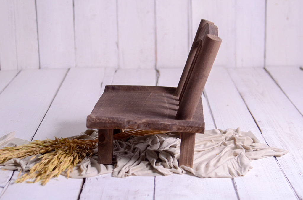 Side profile of mini wide base wooden chair styled on fabric and wheat, rustic newborn photography prop.
