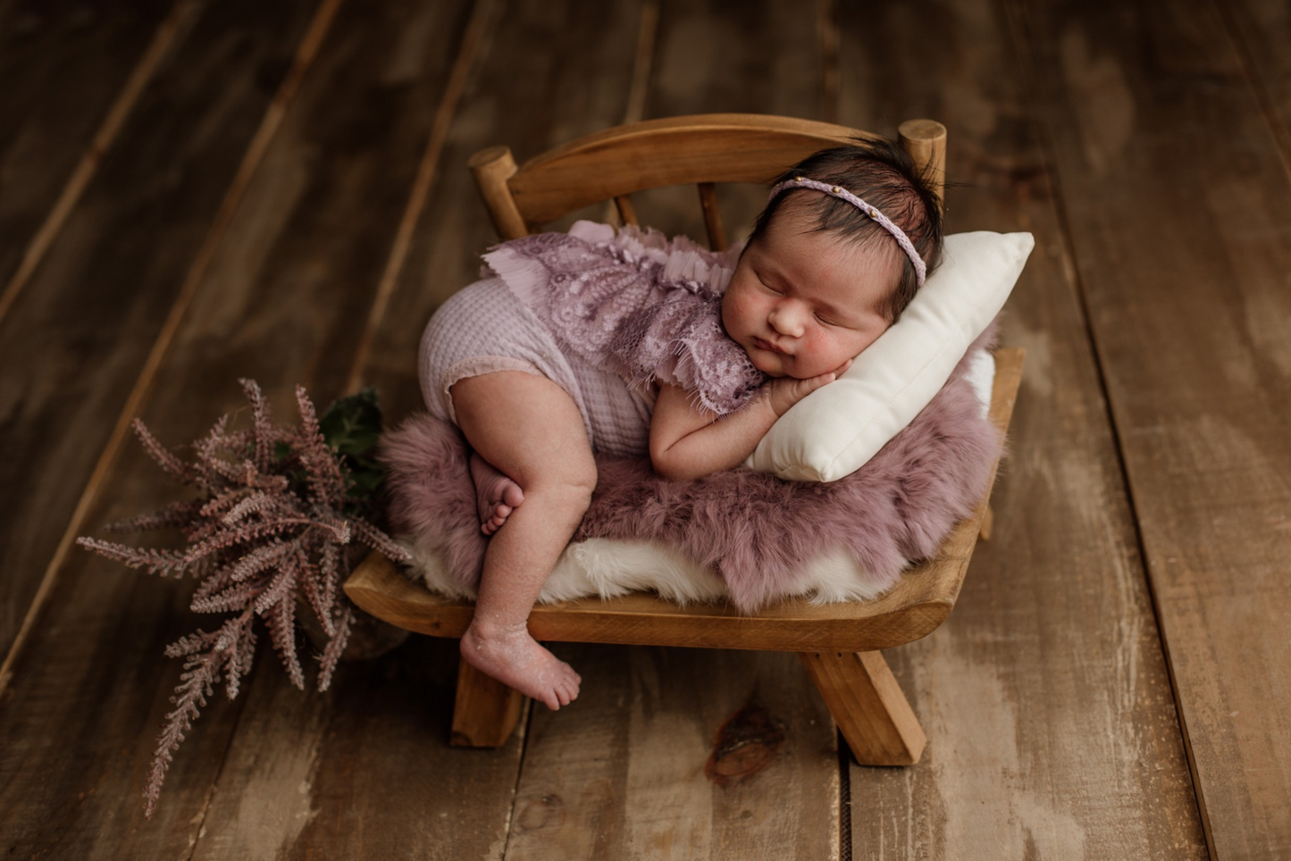 A serene newborn asleep on a fur-draped wooden prop chair, a delicate headband adding charm to this newborn photography prop setup.