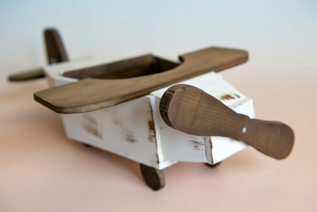 Close-up of rustic wooden airplane newborn photography prop showing brown propeller and wings.