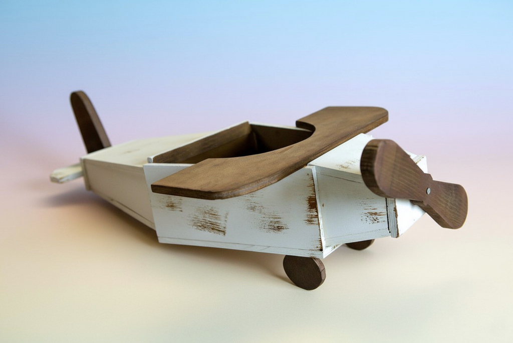 Rustic wooden airplane newborn photography prop with white body and brown wings on wooden floor.
