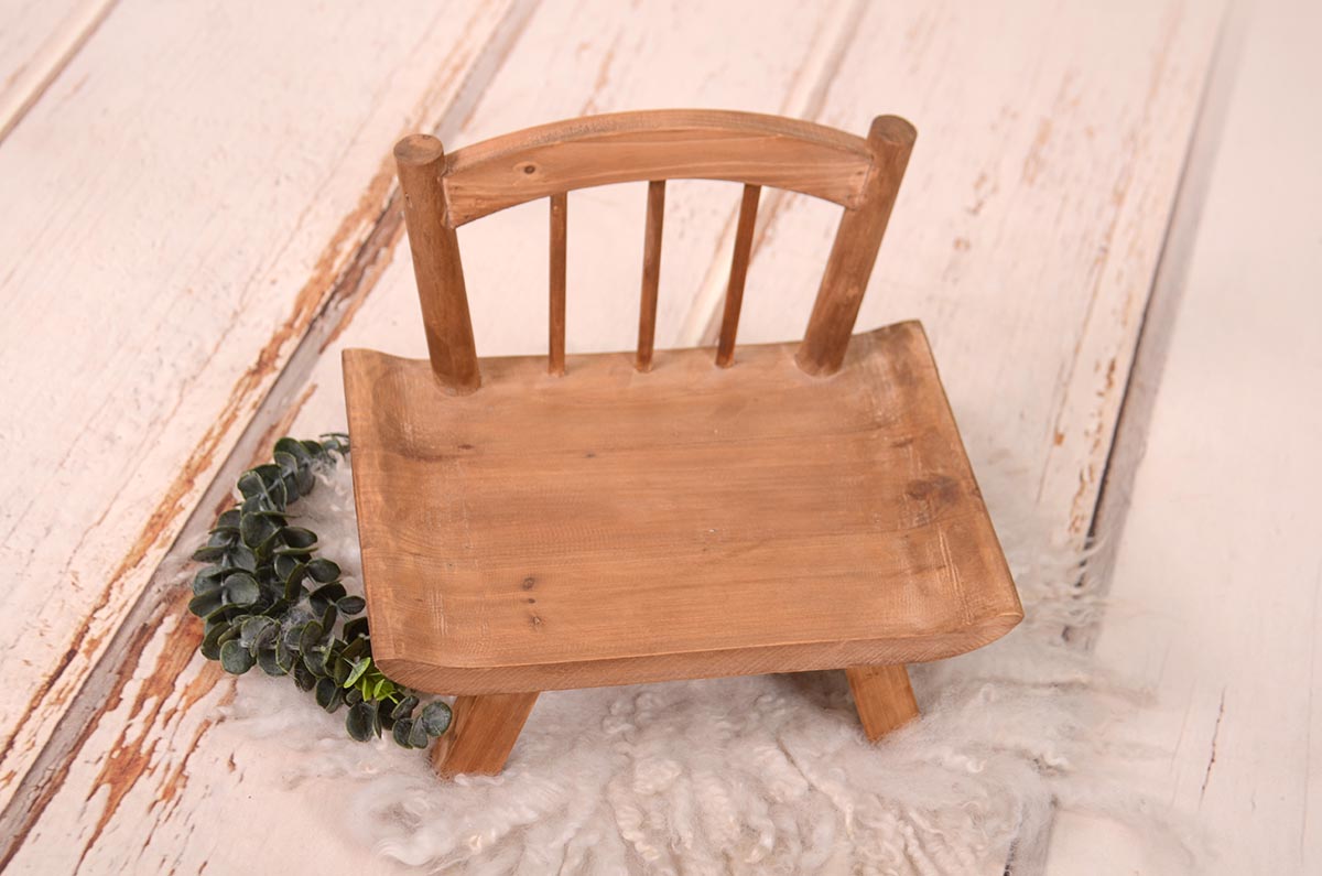 Handcrafted wooden newborn photography prop chair on a fluffy white rug, accented by a greenery sprig, ready for a photoshoot.