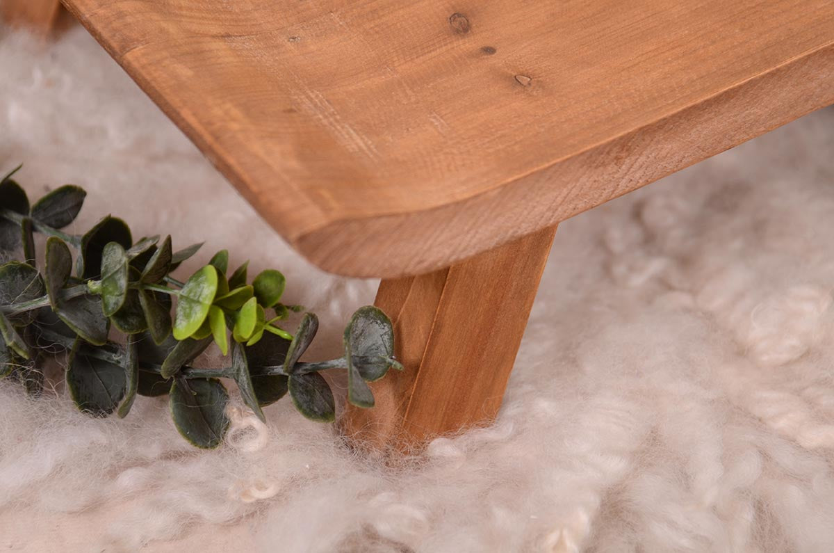 Handcrafted wooden newborn photography prop chair on a fluffy white rug, accented by a greenery sprig, ready for a photoshoot. Closeup