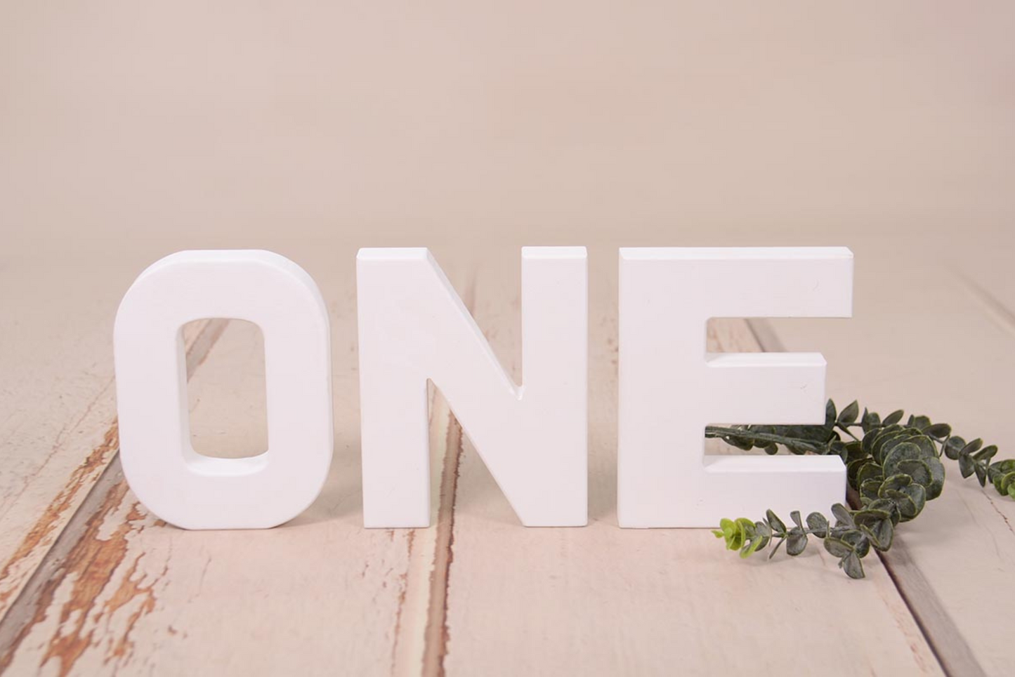 White wooden letters spelling out 'ONE' on a rustic wooden background, ideal for cake smashes or milestone photography.