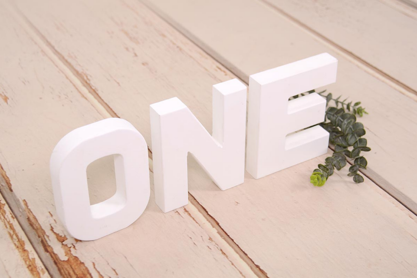 White wooden letters spelling out 'ONE' on a rustic wooden background, ideal for cake smashes or milestone photography.