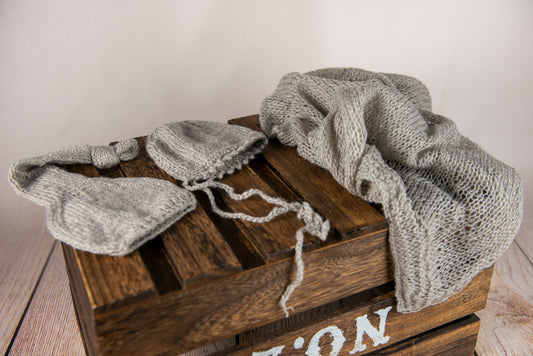 Soft gray bonnet and wrap set displayed as a newborn photography prop on wooden surface.