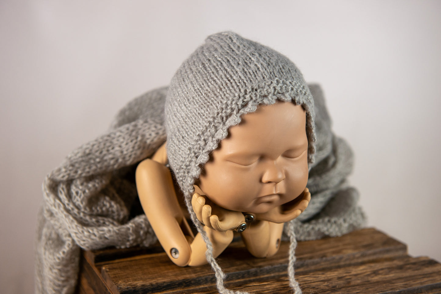 Sleeping doll in gray knit bonnet with matching wrap as cozy newborn photography prop.