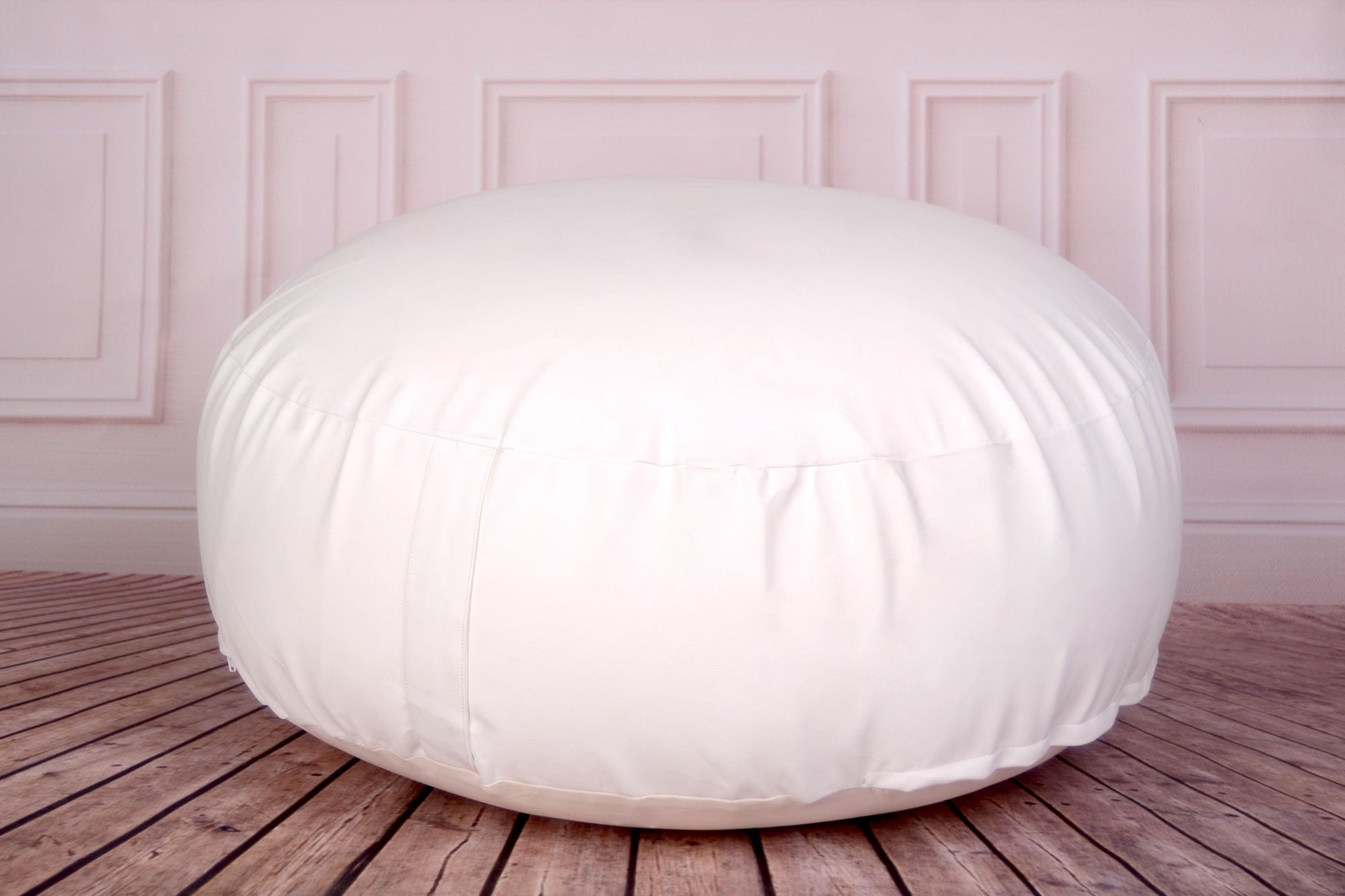 White newborn photography prop beanbag on a wooden floor with elegant wall paneling.