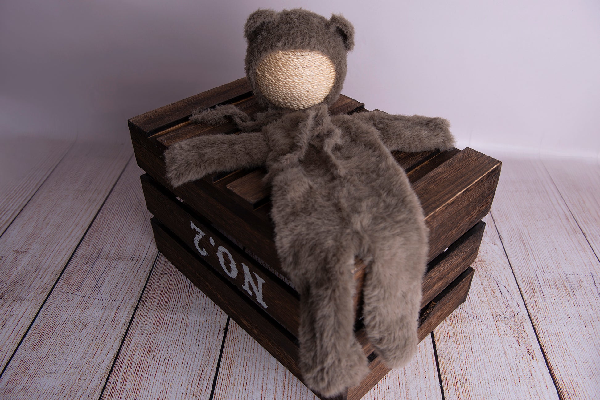 Newborn photography clothing of a bear bonnet and suit in nut brown on a wooden crate.