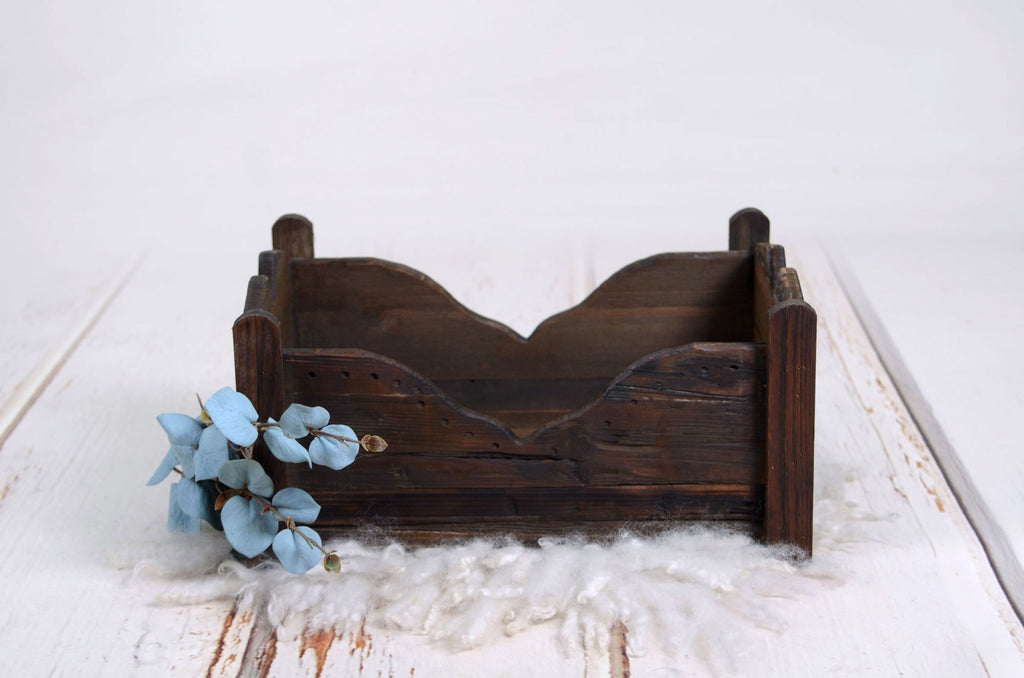 Angled view of a rustic newborn photography prop bed with a wooden bird figurine and blue flowers.