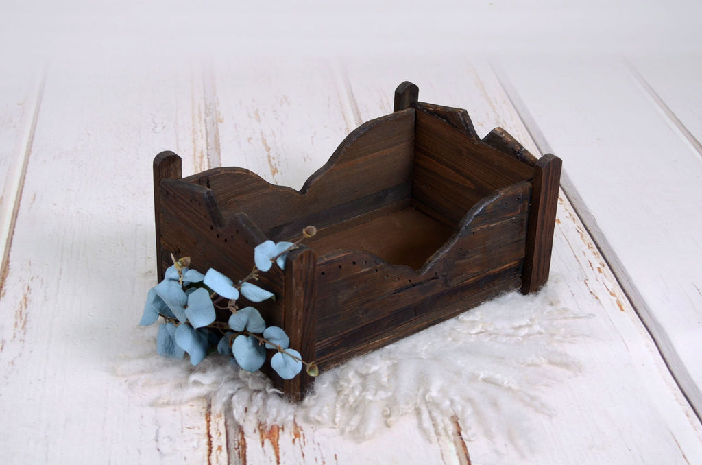 Close-up of a distressed wooden newborn photography prop bed with blue floral accents on a white fur rug.