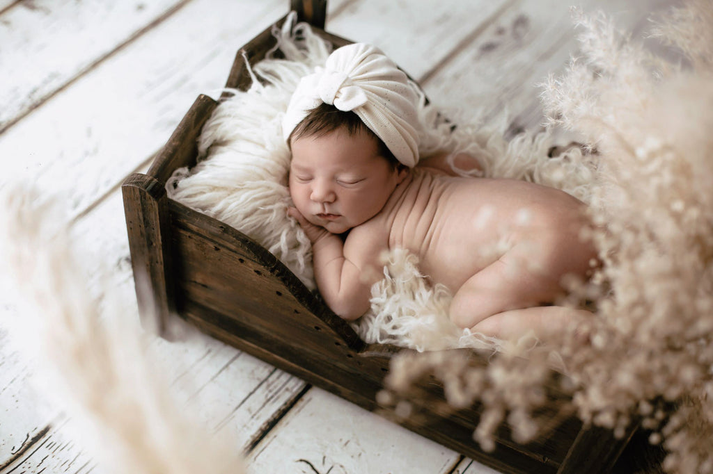Soft-focused image of a newborn wrapped in cream, resting in a rustic bed as a perfect newborn photography prop.