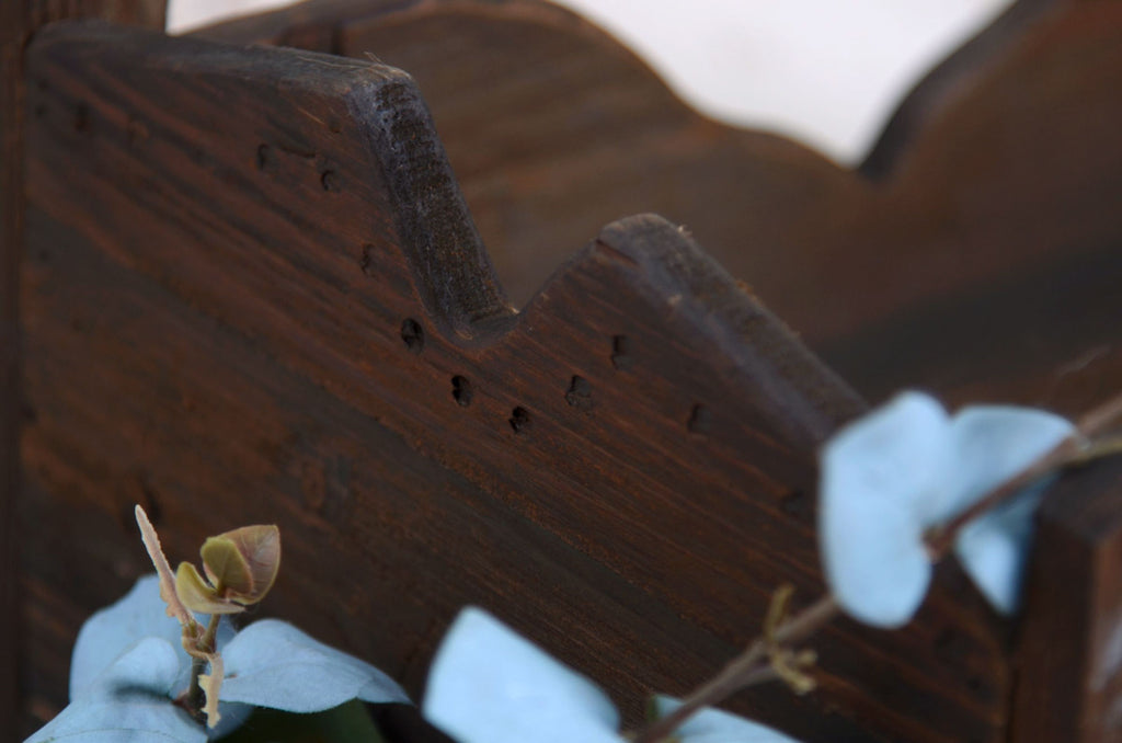 Close-up of the corner of a distressed wooden bed featuring intricate woodwork and a subtle blue flower.