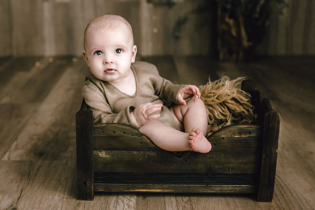 Newborn baby posed on a rustic wooden bed, wearing a delicate beige outfit in a serene newborn photography setup.