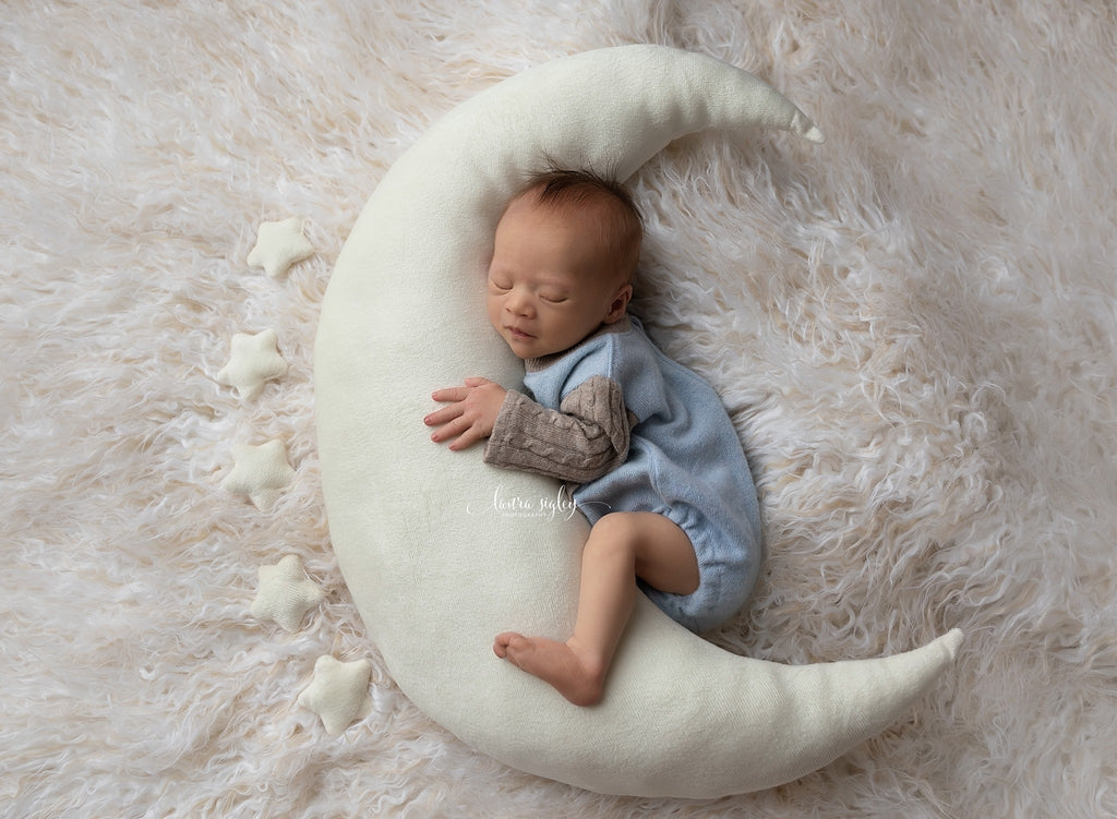 A newborn photography prop featuring a moon-shaped pillow and a baby lying on it with a backdrop of white fur.