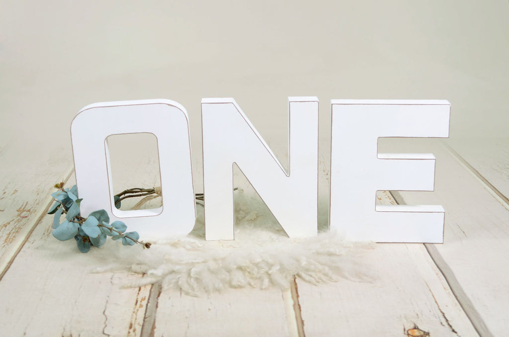 White wooden letters spelling out 'ONE' on a rustic wooden background, ideal for cake smashes or milestone photography.