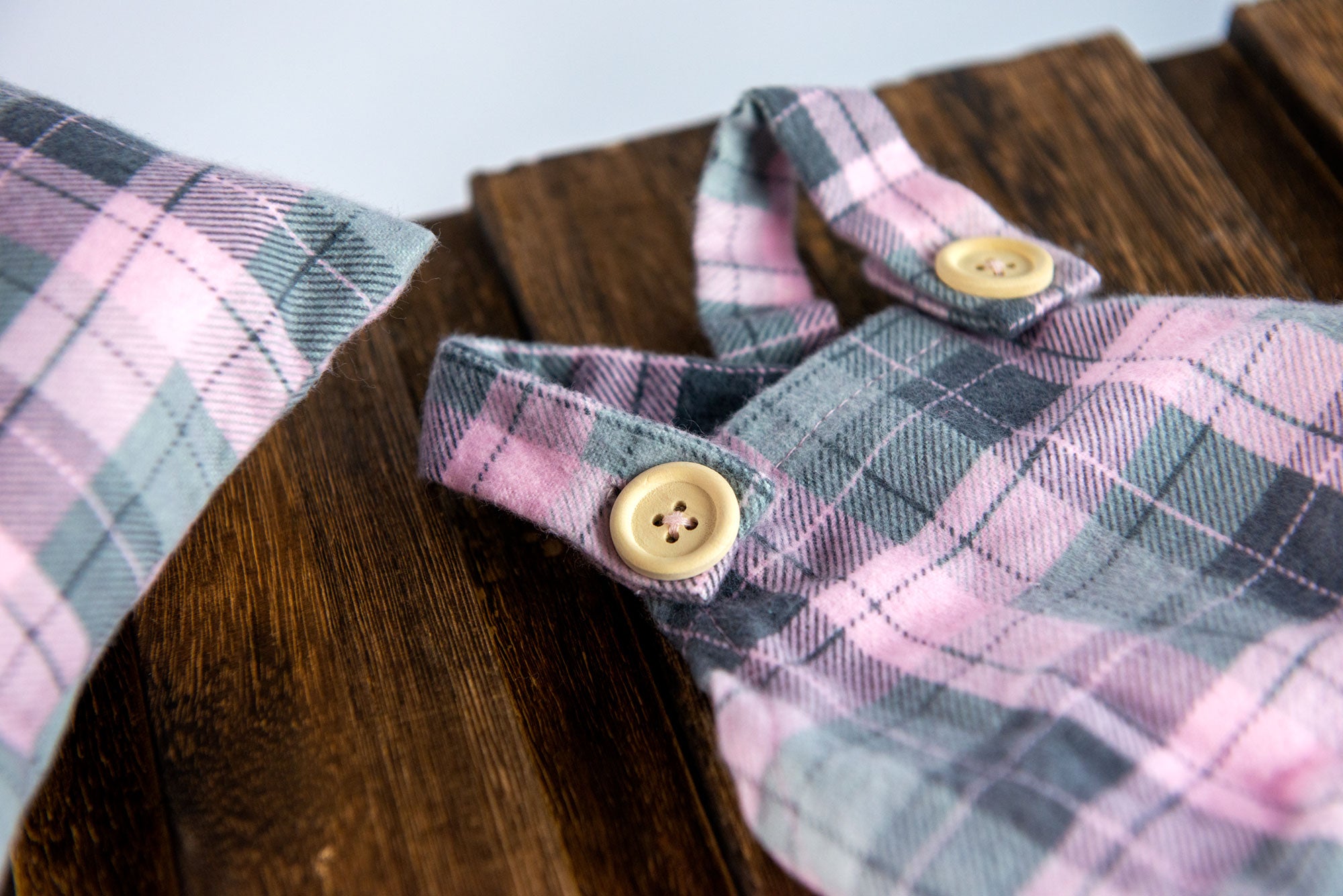 Close-up of pastel plaid newborn photography prop with bonnet and button detail on wooden background.
