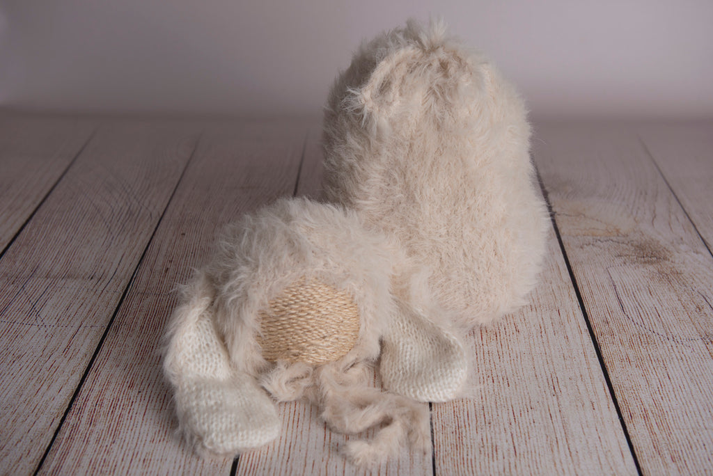 Newborn photography clothing set featuring a beige rabbit ears bonnet and matching sack, displayed on a wooden surface with a soft-focus background.