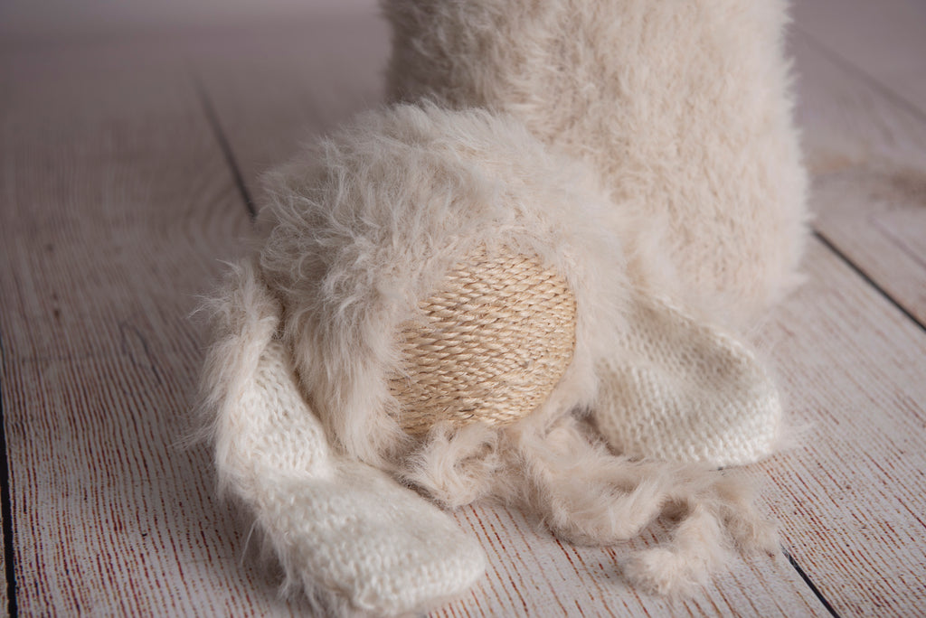 Newborn photography clothing set featuring a beige rabbit ears bonnet and matching sack, displayed on a wooden surface with a soft-focus background.