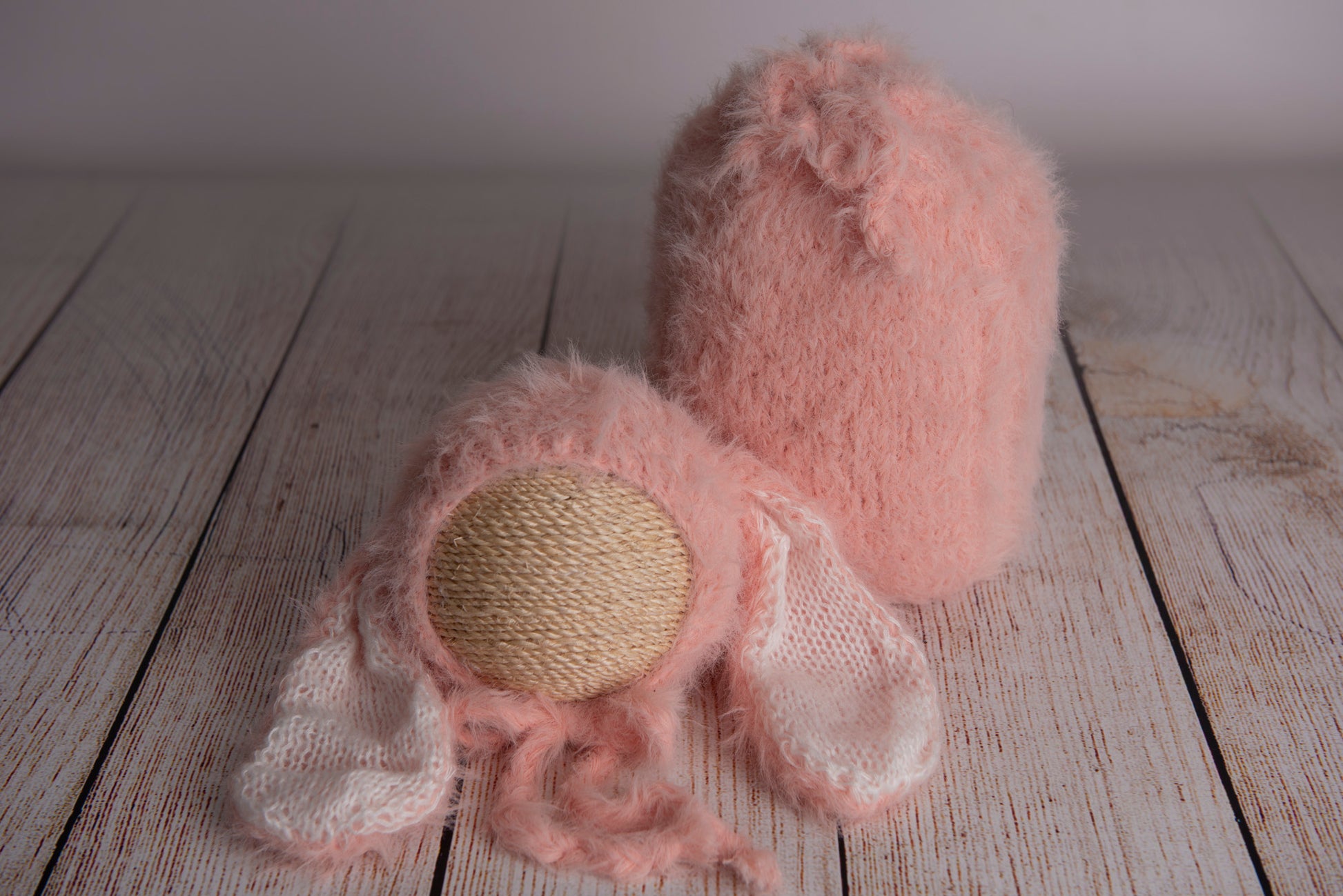 Newborn photography clothing set featuring a beige rabbit ears bonnet and matching sack, displayed on a wooden surface with a soft-focus background.