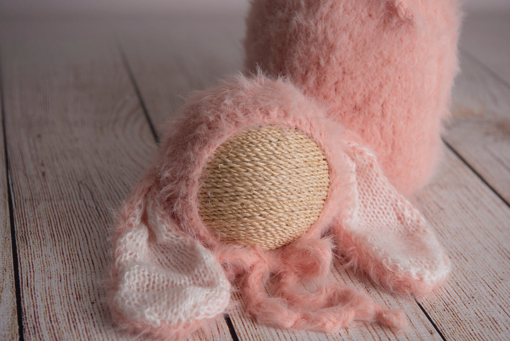 Newborn photography clothing set featuring a beige rabbit ears bonnet and matching sack, displayed on a wooden surface with a soft-focus background.