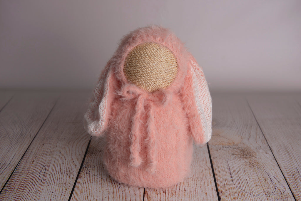 Newborn photography clothing set featuring a beige rabbit ears bonnet and matching sack, displayed on a wooden surface with a soft-focus background.