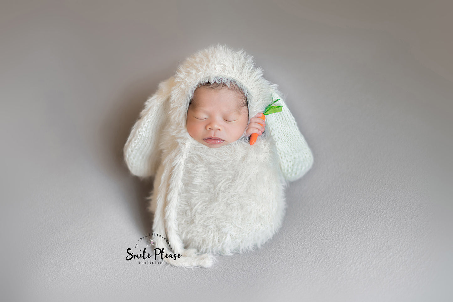 Newborn photography showing a baby in cozy bunny-themed clothing, dozing with a miniature carrot in hand, ideal for capturing the innocence and whimsy of early days.